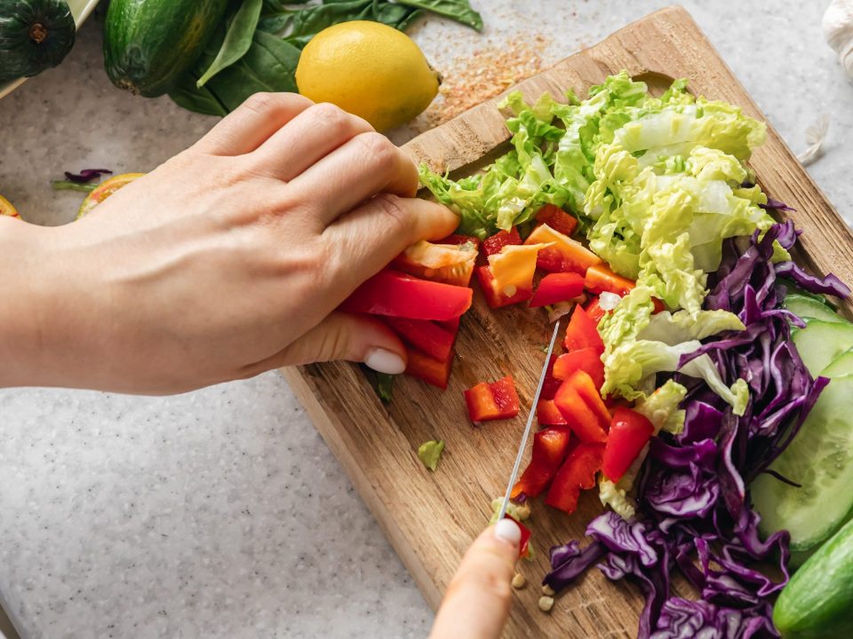 Woman cuts fresh bell pepper wooden board kitchen